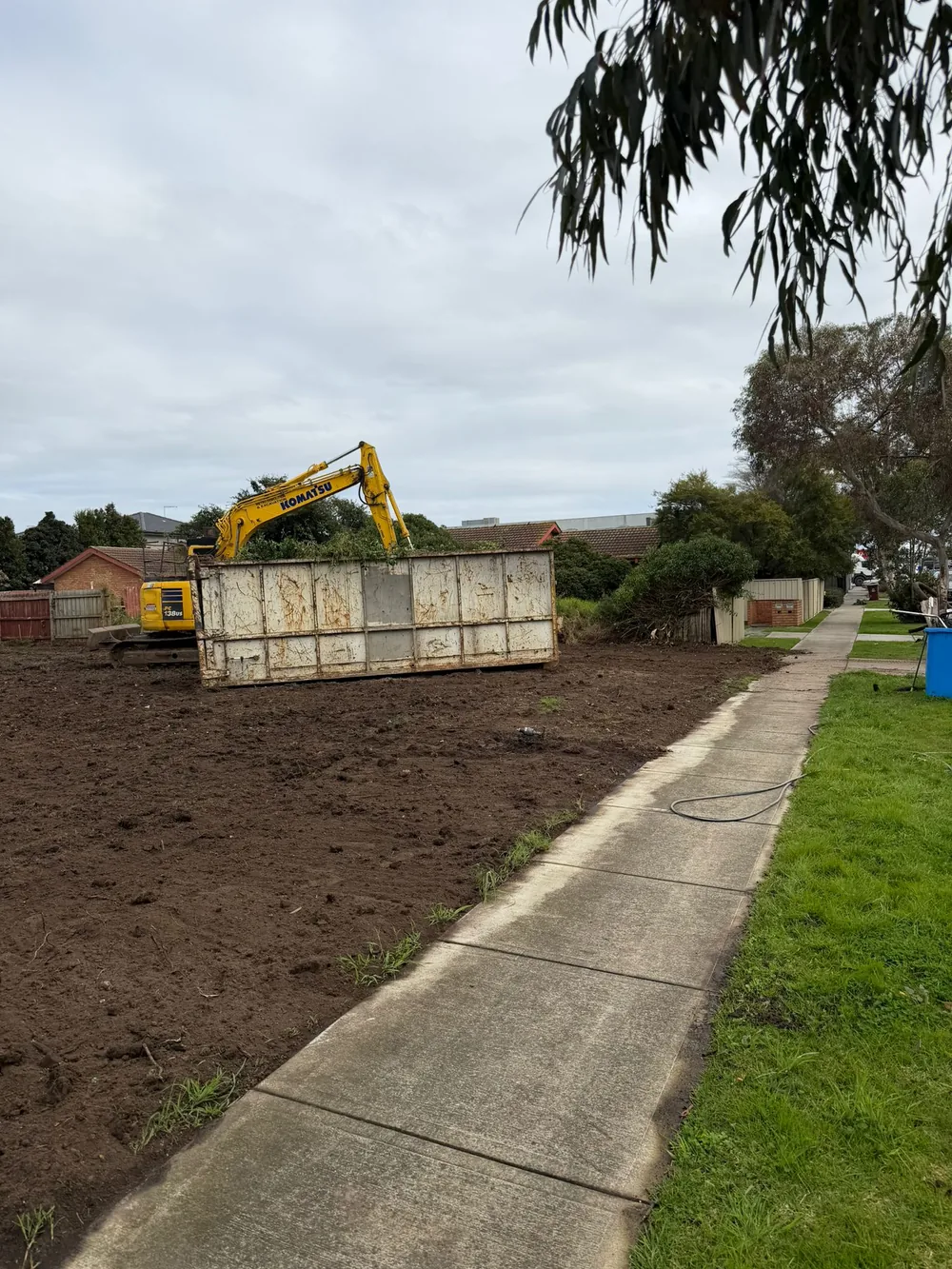 Skip bin and excavator on a cleared block alongside the footpath