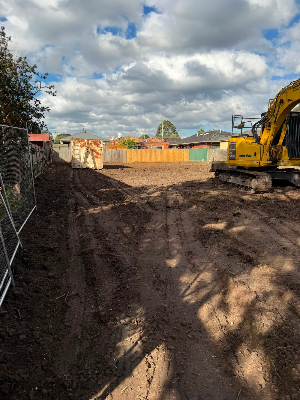 Yellow excavator on a residential site behind temporary fencing