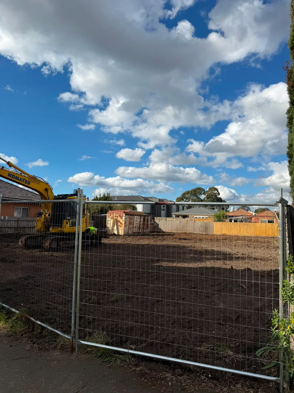 Earthmoving machinery behind a site fence beneath a blue sky